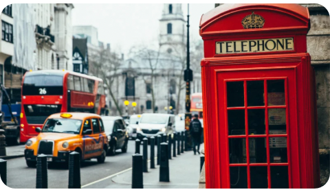 Photo of a street in London, with a classic red telephone cabin at the front, and the iconic London buses in the background.